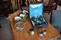 Full view of all items together on wooden table including Royal Grafton cup and bowls in box, silverplate goblets in blue box, glass bowl with silver spoon, brass pitcher, two napkin rings.
