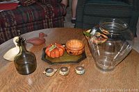 Photo showing carved gourd, ceramic pumpkin, ceramic bowl with papermâché vegetables, pottery duck figurines, Norwegian bird dishes, smoked glass decanter, and large glass vase on wooden table