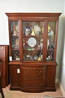 Full front view of the wooden Duncan Phyfe china cabinet with glass door showing interior items, drawers, and side doors