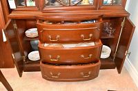 Wooden display cabinet with drawers open showing stacked glass bowls, china plates, and glass dishes inside