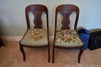 Photo of two wooden chairs with needlepoint floral seats, showing front views and details of upholstery and wood finish.