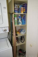 Full shelf with cleaning supplies and accessories beside washer and dryer