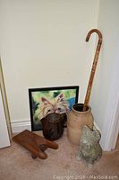 Six decor items grouped against wall: framed dog print, brown pitcher, beige vase with cane, wooden boot remover, and dog statue in front.