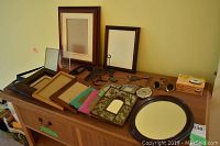 Wide shot showing 13 picture frames in various sizes and styles, an oval framed mirror, and the Sonic Boom alarm clock on a dresser.