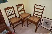 Three wood and wicker chairs, two matching with spindle backs, one ladder-back chair, all show wear and some broken cane seating.
