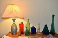 Photo of a table lamp and 8 decorative glass bottles on a wooden table