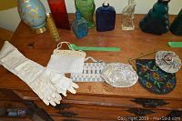 Photo showing two pairs of cream leather gloves and five different clutch purses arranged on a wooden surface.