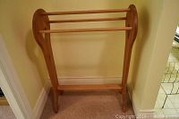 Wooden towel rack against wall showing full rack with three horizontal wooden rods for hanging towels or linens.