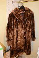 Full view of the brown otter fur coat hanging on a black hanger, showing the texture and length of the coat.