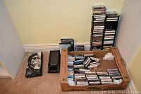 Wide view showing box with assorted cassette tapes and plastic holder with stacked tapes and DVDs