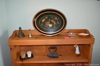Photo of top shelf including hand-painted oval floral tin tray, brass figurine bell, small brass bell, small glass bowl, and white ceramic bowl with scalloped edges.
