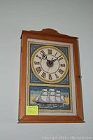 Wooden framed needlepoint wall clock with Roman numerals and sailing ship needlepoint design at bottom.