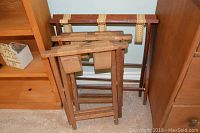 Three wooden luggage holders leaning against a wall, showing their wooden frames and fabric straps.