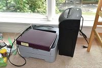 Side view of Brother HL-2170W printer and Omnitech shredder on carpet with natural light from window.