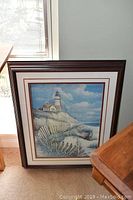 Photo of shadow box artwork featuring lighthouse scene with boat and coastal natural elements.