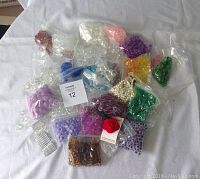 Photo showing multiple small plastic bags with beads of different colors and materials laid out on a white cloth.