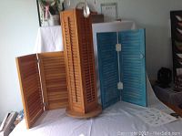 Photo showing three jewelry displays made from vintage shutters. Two with natural wood finish and one turquoise blue. One display is rotating with four sides for hanging jewelry.