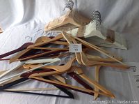 31 wooden hangers in different finishes and styles piled together on white fabric.