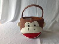 Front view of the sock monkey fabric basket showing the smiling face, ears, and handle on a neutral background.