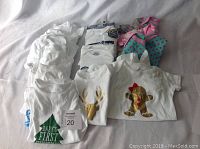 Photo showing a collection of white and colored baby onesies, some with vinyl iron-on images like green 'Baby's First', gold deer head, and gingerbread man.