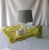 Photo showing the glass lamp with teal blue paisley lampshade, chartreuse green throw, green ceramic owl candle holder, and white ceramic wax melter arranged on a table.