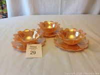 Photo of set of three vintage dessert bowls with matching saucers arranged on table, showing scalloped petal edges and iridescent orange glaze.