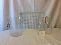 Photo of clear acrylic wine bucket, three clear glass wine carafes, and white wire serving tray with wooden handles all placed against a white backdrop.