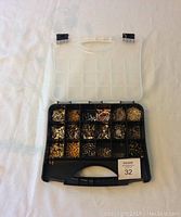 Top-down view of open black plastic storage container with transparent lid showing multiple compartments filled with assorted jewelry making findings and charms in various metal tones.