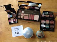 Photo showing multiple makeup palettes and skincare containers on wooden surface.