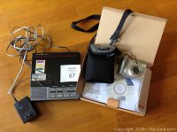 Photo showing Canon PowerShot A530 digital camera with case, cables, manuals, software CD, next to a black older digital answering machine with remote control and power adapter.