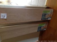 Two new wooden stair riser DIY kits, unfinished wood panels, stacked vertically against a wall with visible product labels.