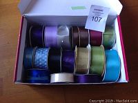 16 rolls of satin ribbon in various colors and some patterned shown inside an open box