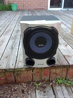 Sony D.S.W. subwoofer speaker placed on outdoor wooden deck, photographed from front showing speaker grille, dual bass reflex ports, and Sony branding.