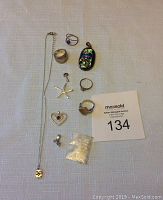 Overview of lot with eleven silver jewelry items displayed on a cloth surface, including rings, pendants, a necklace, and a small bag of beads.