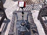 Metal wire merchandise display stand with circular arms and round black base on outdoor glass table.