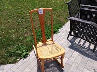 Antique wooden rocking chair with cane seat outdoors on pavement showing full chair and backrest detail