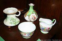 Four small china items on wood shelf including candle holder, bud vase, creamer, and sugar bowl
