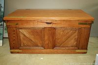 Front view of solid oak blanket box with hinged lid closed showing panelled front and brass hardware