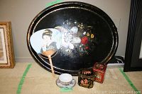 Wide angle view of full lot including black lacquered tray, paper fan, two tins, cup and saucer arranged on carpet