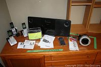 Philips micro hi-fi system, VTech cordless phones, Sony Dream Machine radio, TomTom GPS with manuals and accessories on wooden surface.