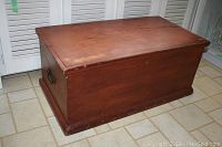 Front and top view of the antique wooden chest showing the flat lid and metal side handle.
