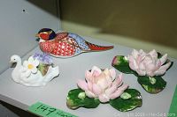 Display shelf showing large hand painted bird, white swan with flowers, and two pink lotus flower figurines.