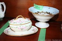 Two Limoges porcelain pieces on display, showing the covered dish with underplate and pedestal bowl with floral design and gold detailing