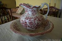 Pitcher and bowl set displaying red floral pattern on semi-porcelain with scalloped edges, on table indoors