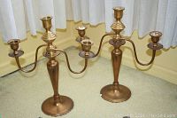 Pair of brass candelabras standing side by side on floor showing overall design and size.
