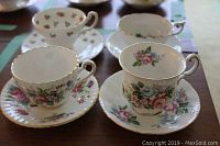 Four teacups and matching saucers with floral patterns and gold trim arranged on a table.