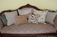 Seven assorted throw pillows arranged on a vintage patterned sofa with wooden carved frame.
