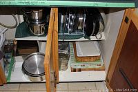 Inside cabinet shelf with stacked pots, pans, bakeware and cutting boards showing a variety of kitchen items including round cake pans, rectangular pans, and cutting boards stacked together.