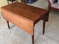 Photo of wood drop leaf table with one side leaf down and one up, showing turned legs.