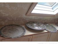 Three silverplate trays and platters arranged on a wooden shelf under a skylight, showing their size and overall condition.
